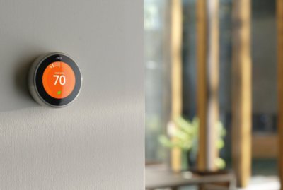 Smart thermostat mounted on wall displaying seventy degrees farhenheit