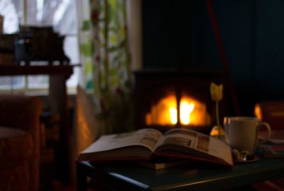 Open book on table next to tea cup in front of a fireplace